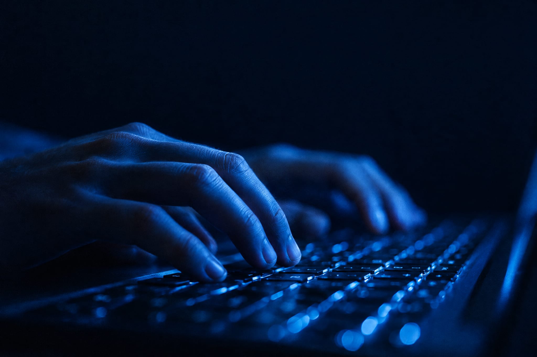Close-up of hands typing on a laptop at night, lit by the screen’s glow